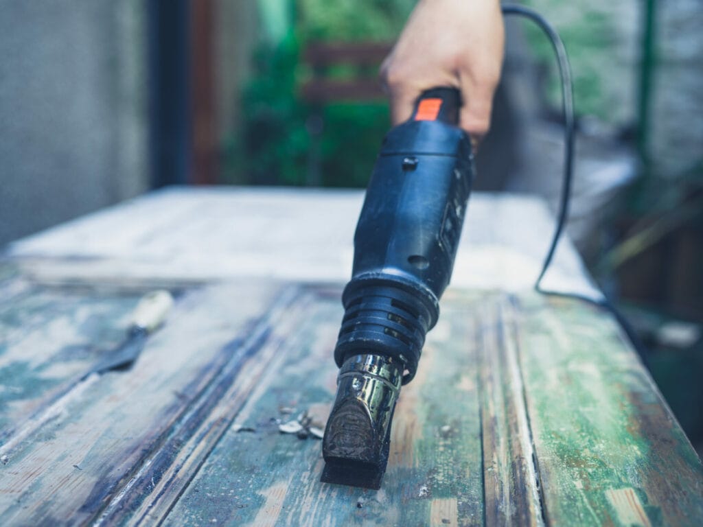 The hand of a young man stripping paint from a door with a heat gun